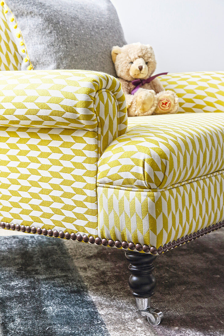 Teddy bear sitting on armchair with yellow and white graphic pattern on cover