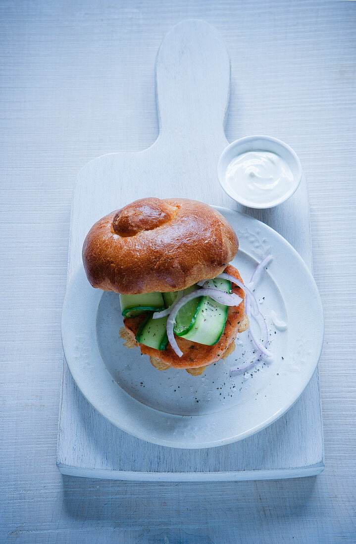 A salmon burger with a brioche bun, cucumber and onions