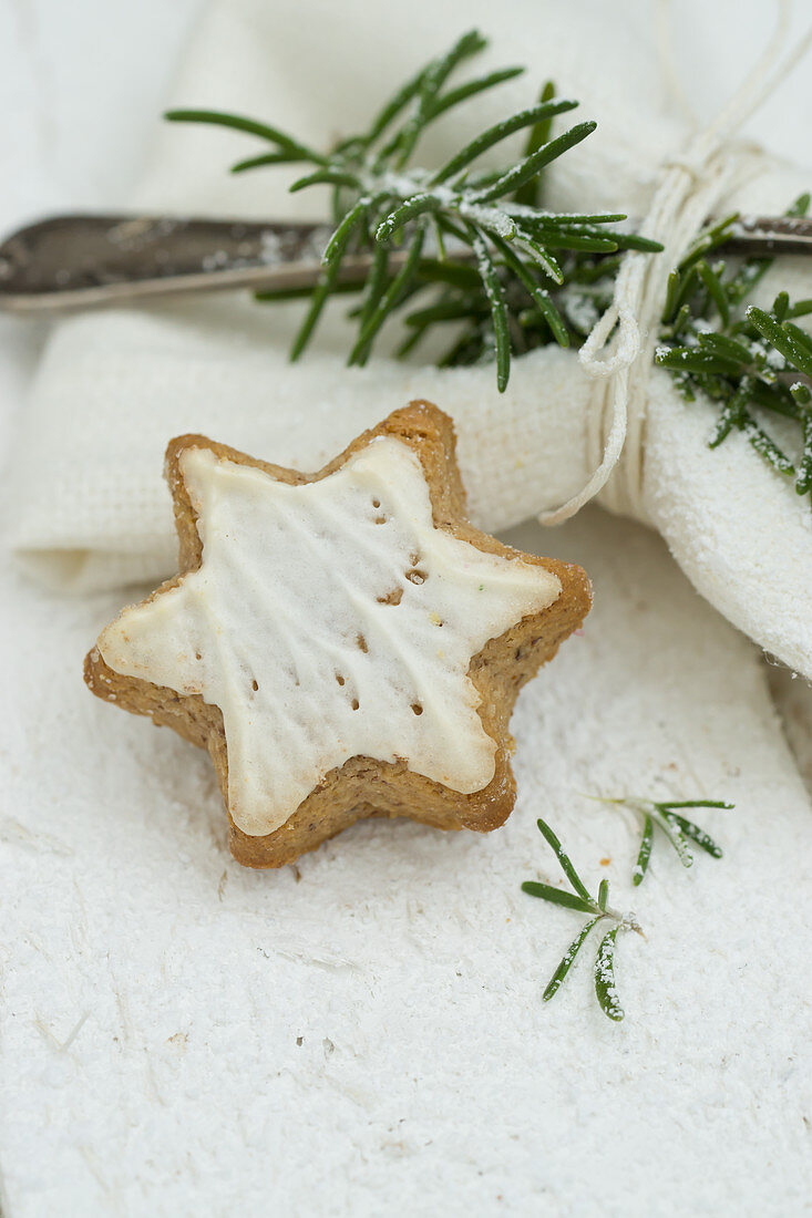 A cinnamon star next to a napkin with a silver fork and a sprig of rosemary