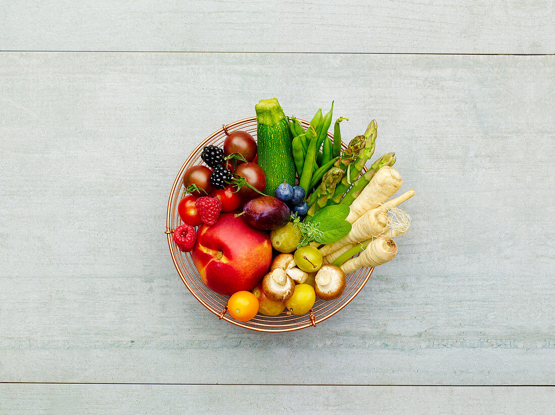 Fresh, colourful fruit and vegetables in a wire basket (seen from above)