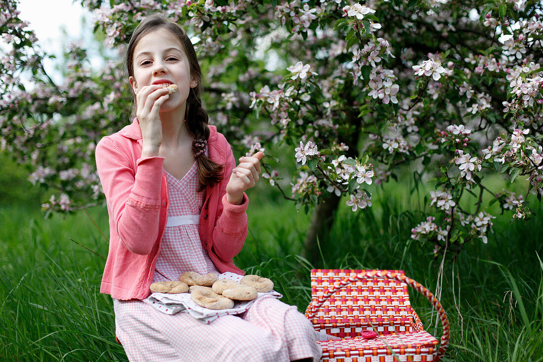 A girl having a picnic in a meadow amongst apple trees