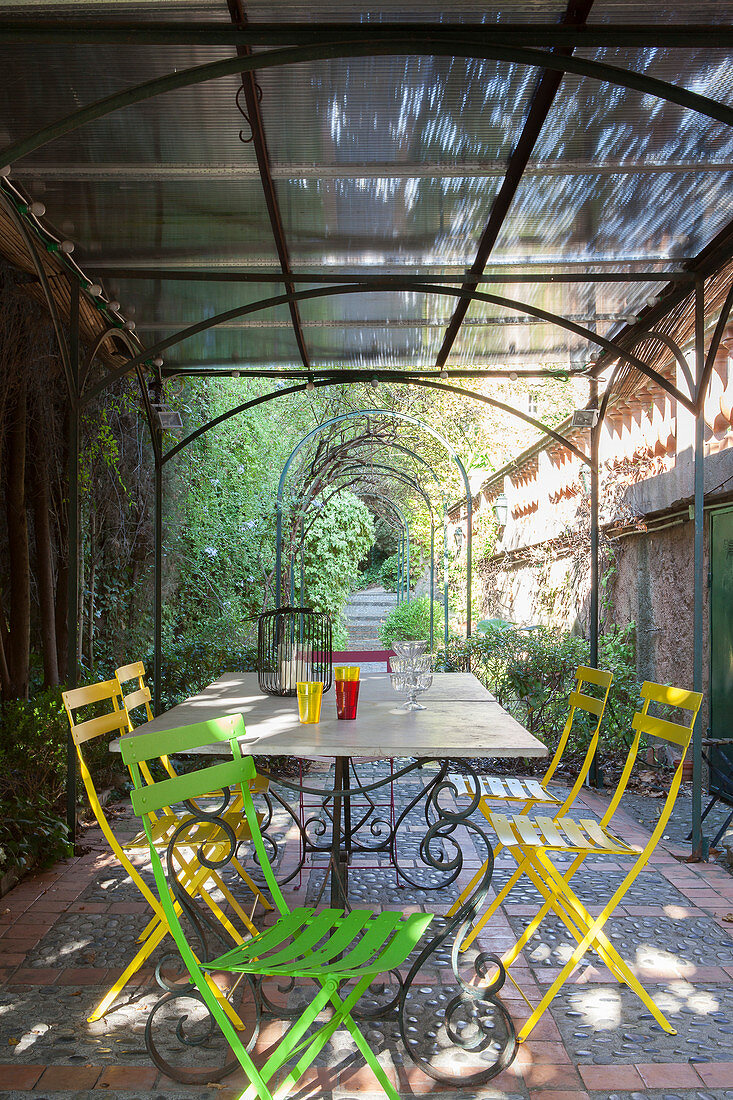 Bunte Gartenstühle um einen Metalltisch auf mediterraner Terrasse