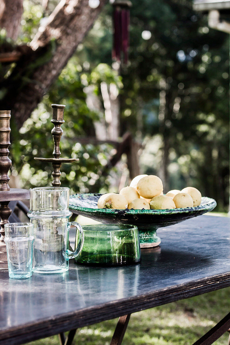 Garden table with glasses and fruit bowl under tree