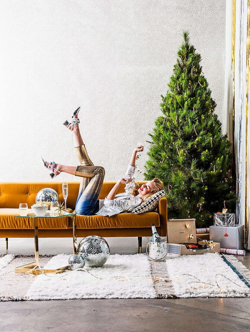 Blonde Frau auf ockergelbem Sofa liegend vor Weihnachtsbaum