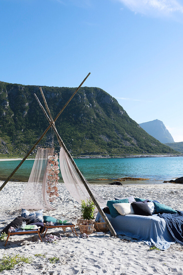 Wigwam decorated with shells and bed linen and pillows in shades of blue on bed on beach