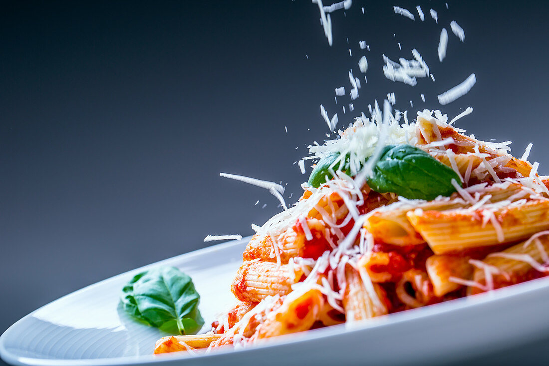 Käse rieselt auf Penne mit Tomatensauce und Basilikum