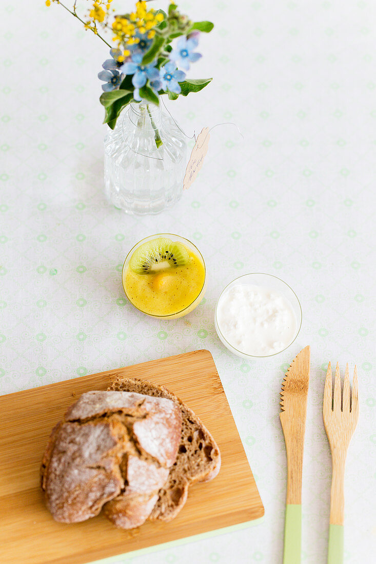 Holzbesteck, Brot auf Holzbrettchen, Mangopuree und körniger Frischkäse