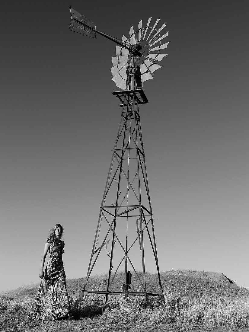 A young woman wearing a long summer dress standing next to a wind turbine (black-and-white shot)