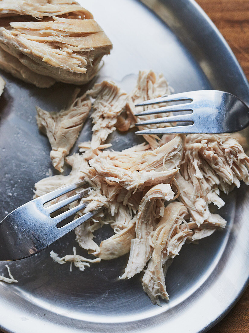 Chicken being shredded with forks