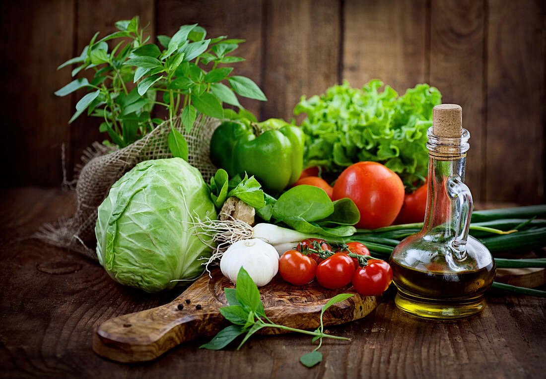 Stillleben mit frischem Gemüse, Kräutern und Olivenöl in Karaffe