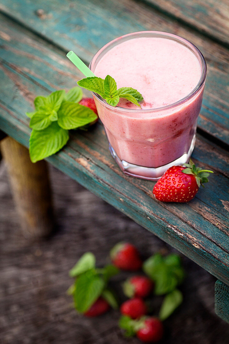 A strawberry smoothie outside on a wooden bench