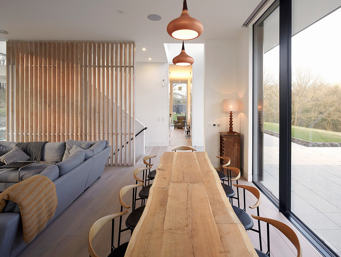 Long wooden table in open-plan interior next to glass wall overlooking terrace