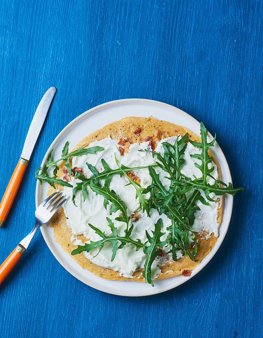 A pancake with dried tomatoes and rocket