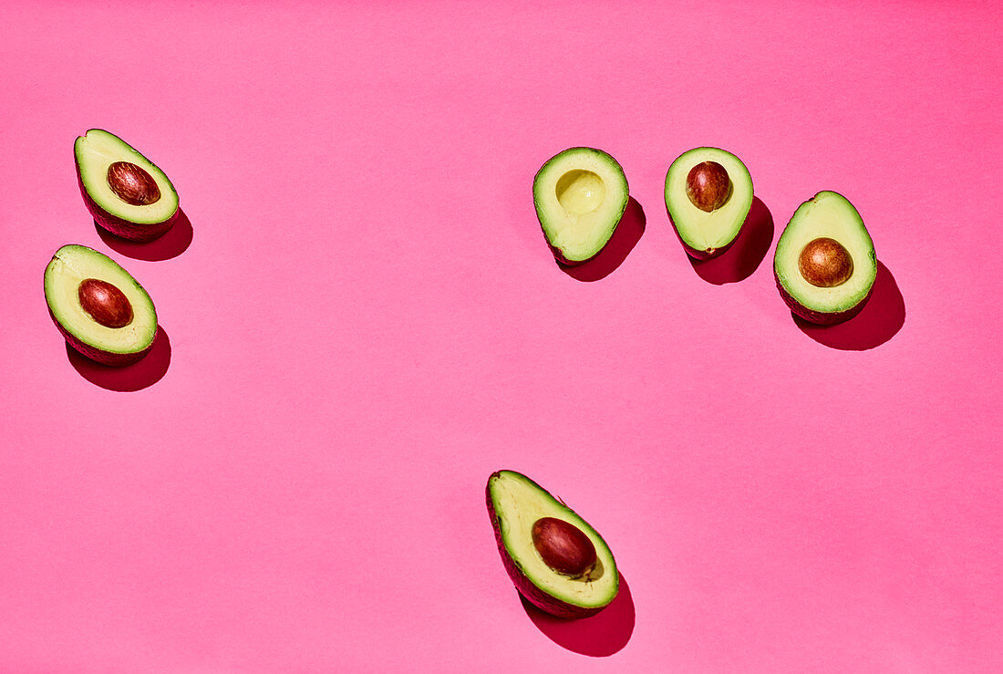 Avocado halves on a pink surface