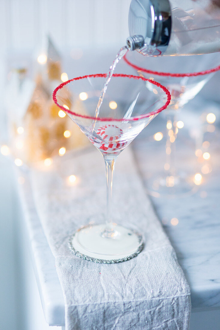 A drink being poured into a Martini glass over a Christmas bonbon
