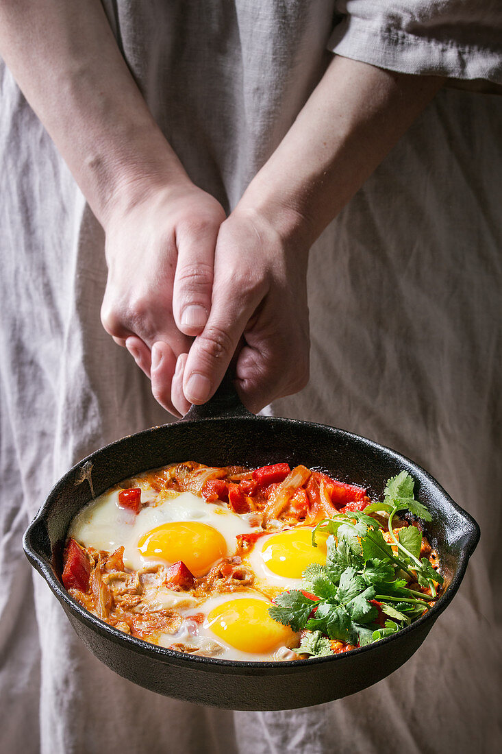 Traditional Israeli Cuisine dishes Shakshuka (Fried egg with vegetables tomatoes and paprika in cast-iron pan in female hands)