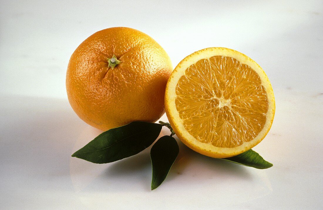 Eine halbierte und eine ganze Orange auf drei Orangenblättern