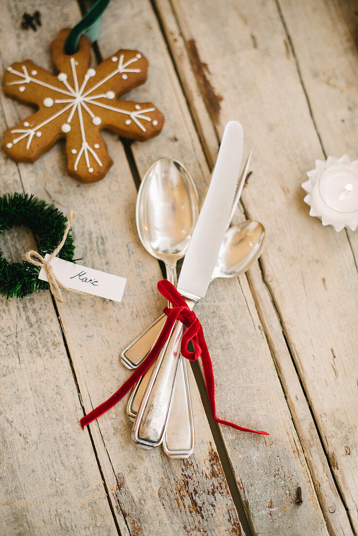 Silver cutlery tied with red velvet ribbon and gingerbread biscuit on wooden surface