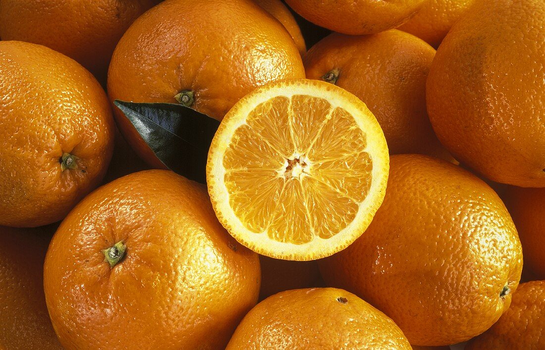 Eine Orangenscheibe liegt auf ganzen Orangen
