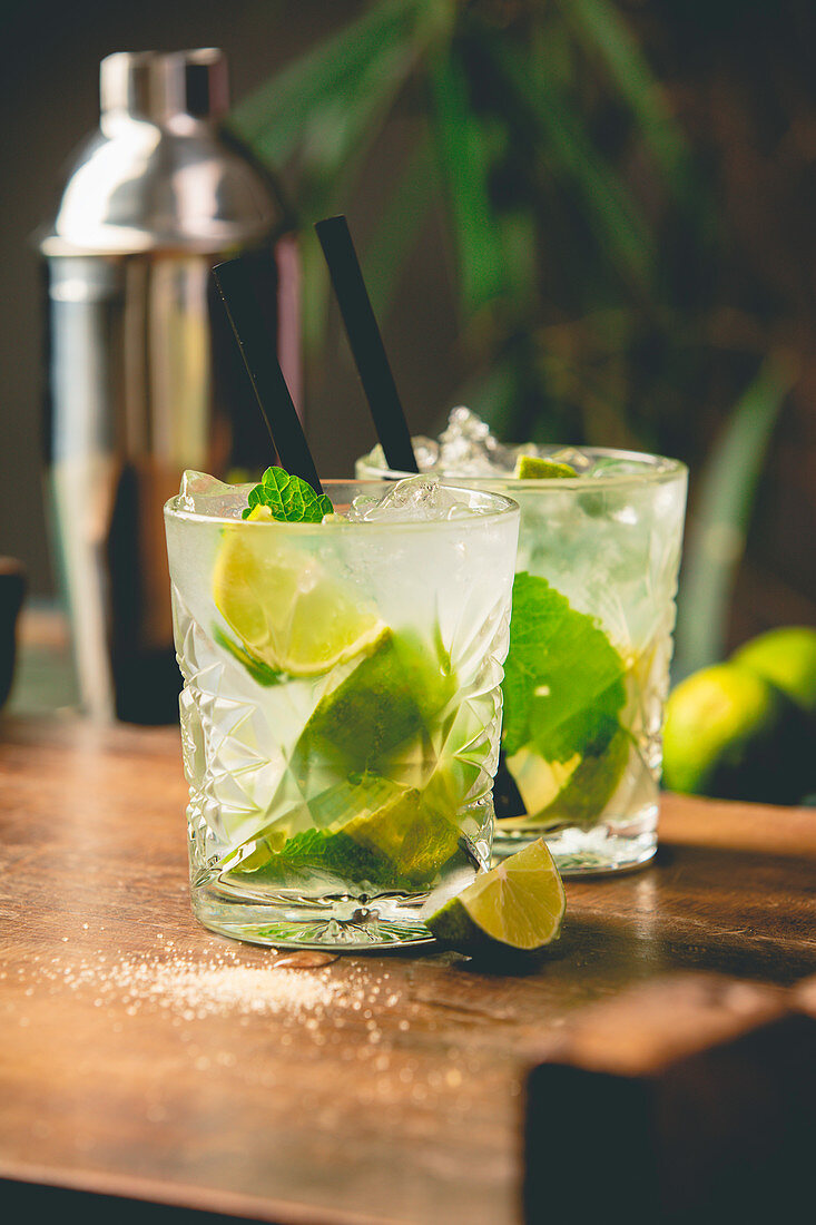 Two glasses of mojito cocktail with fresh lime and mint on a wooden table