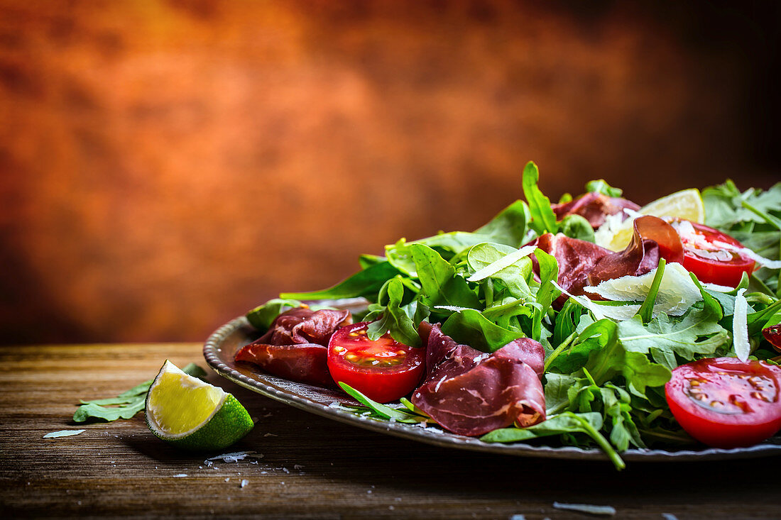 Salad bresaola with arugula, baby spinach, tomatoes, lime and cheese parmesan