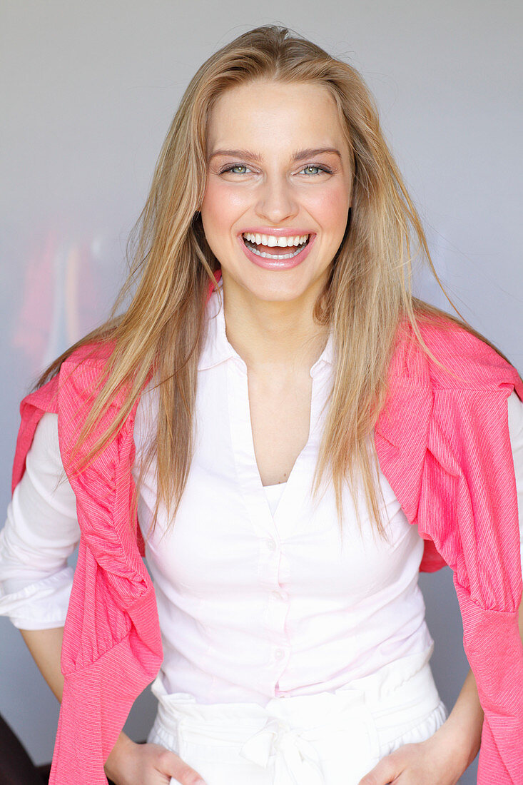 A young woman wearing a white shirt with a pink jumper over her shoulders