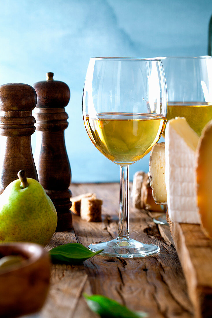 An autumnal arrangement of white wine, cheese, pears, a salt and a pepper mill