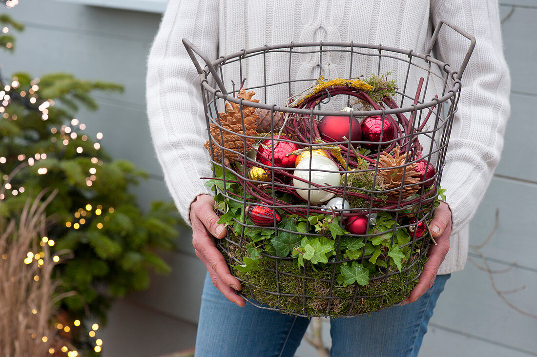 Woman bringing wire basket with Christmas baubles, cones and moss