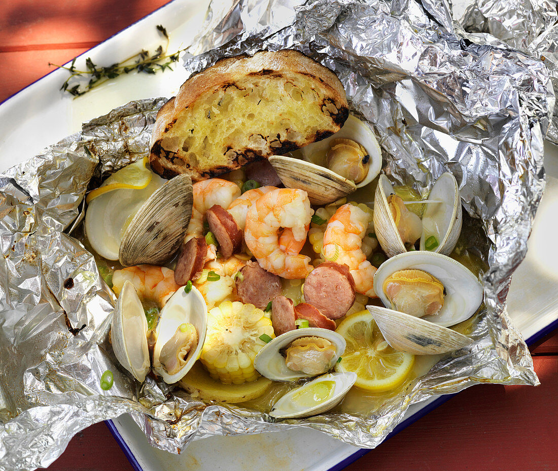 Seafood cooked in foil with corn on the cob and grilled bread