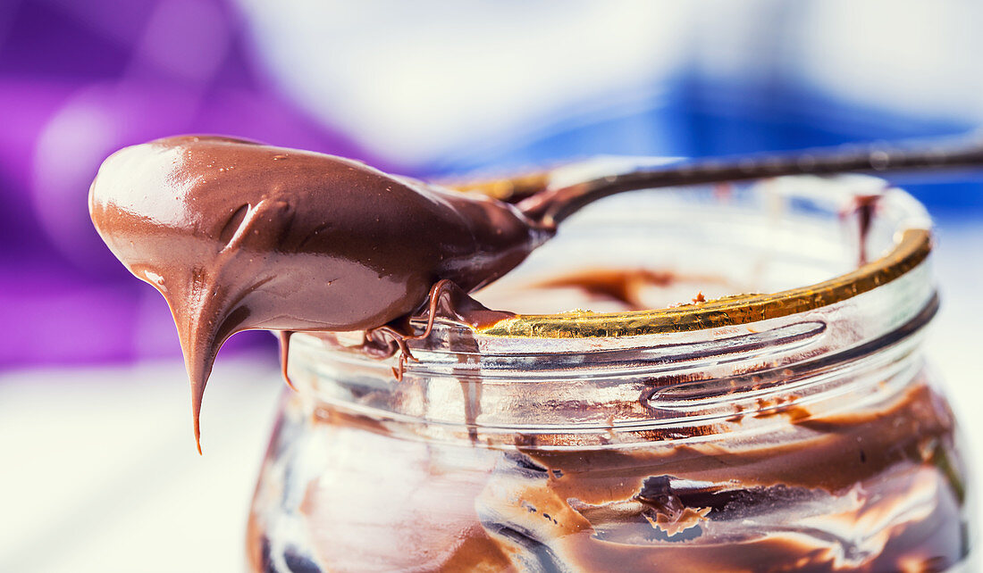Löffel und Glas mit Schokoladen-Haselnuss-Aufstrich