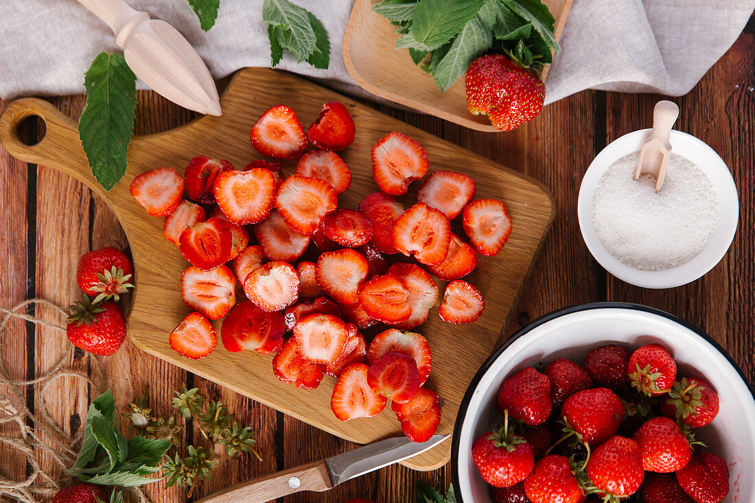 Frische Erdbeeren, teilweise geputzt und geschnitten und Zucker