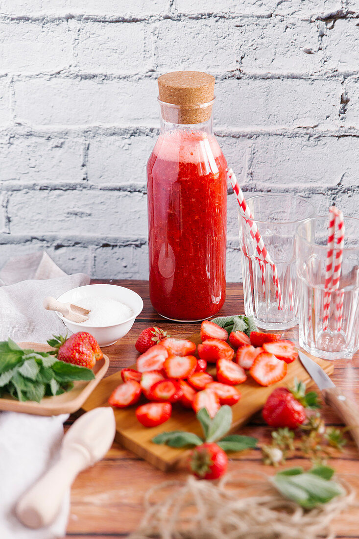 Eine Flasche mit Erdbeersmoothie und geschnittene Erdbeeren auf Holzbrett