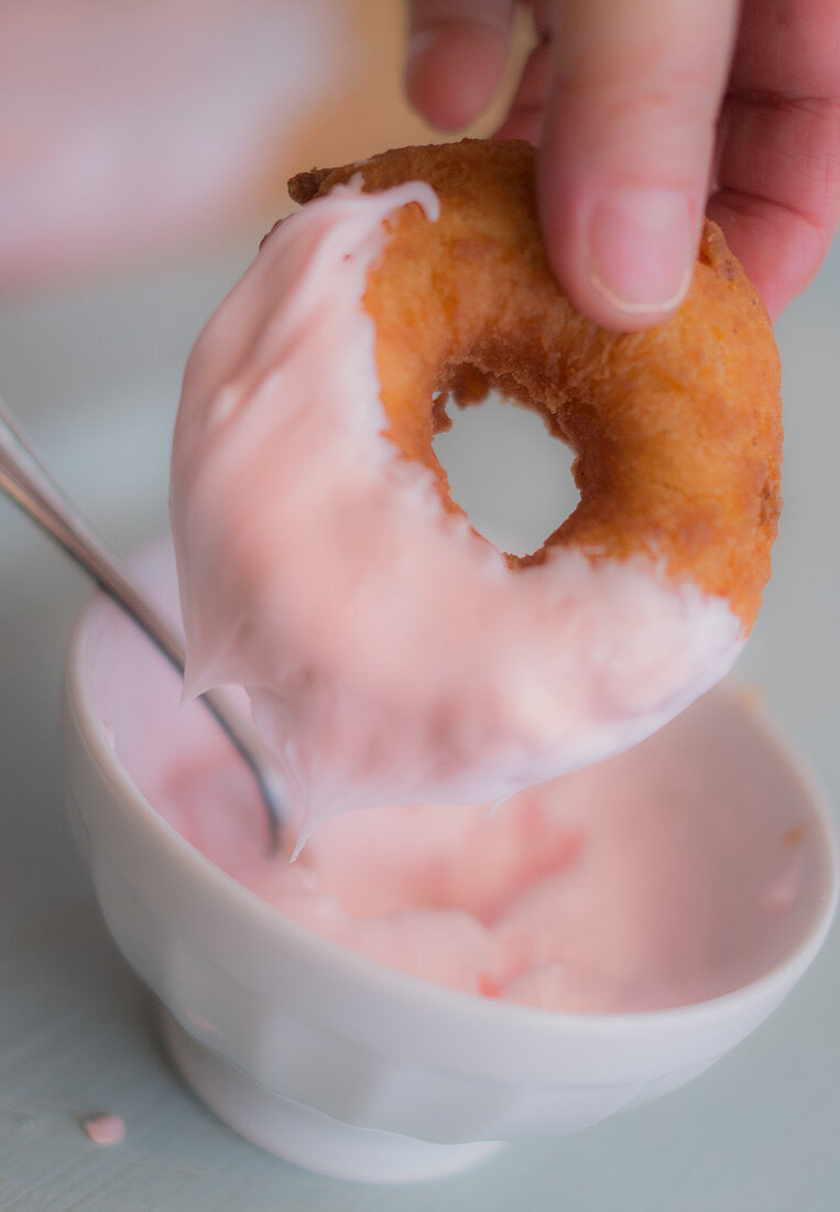 Donut wird mit rosafarbenem Zuckerguss glasiert
