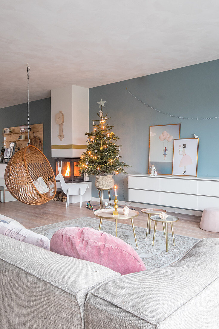 Hanging chair and Christmas tree in front of fire in living room with blue wall
