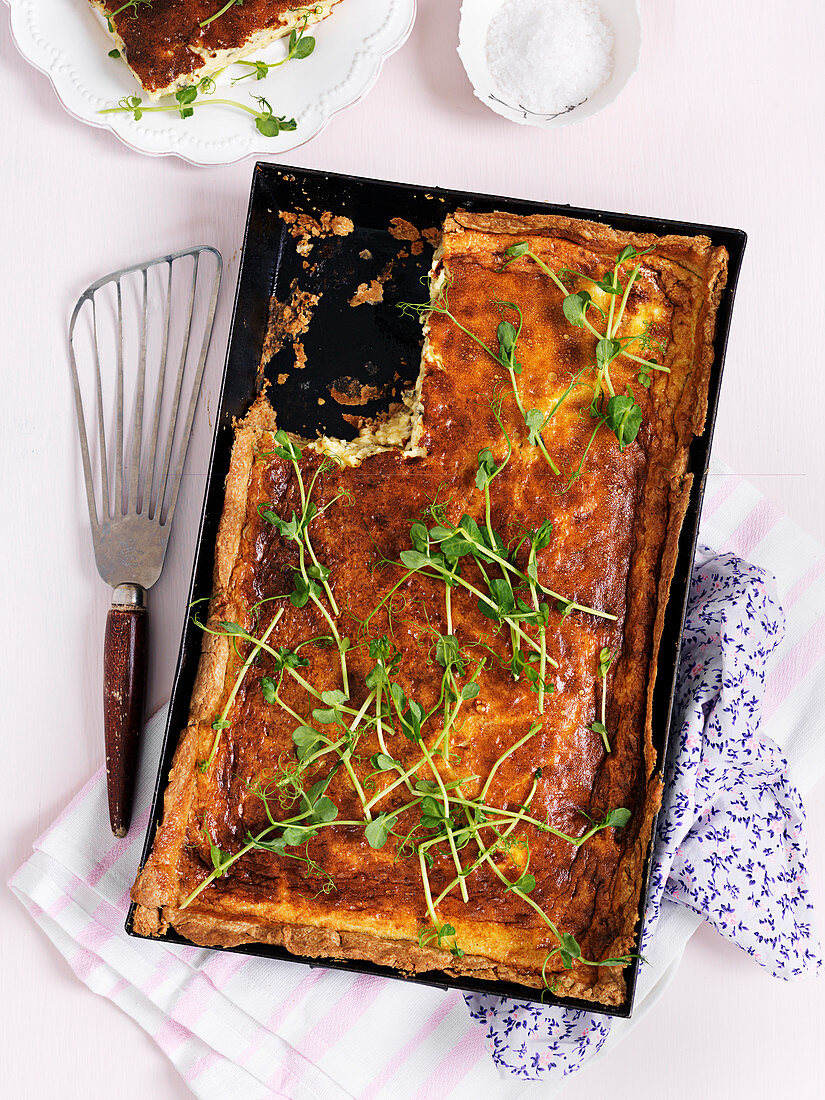 Cheese quiche in a metal baking tray sprinkled with pea sprouts (top view)