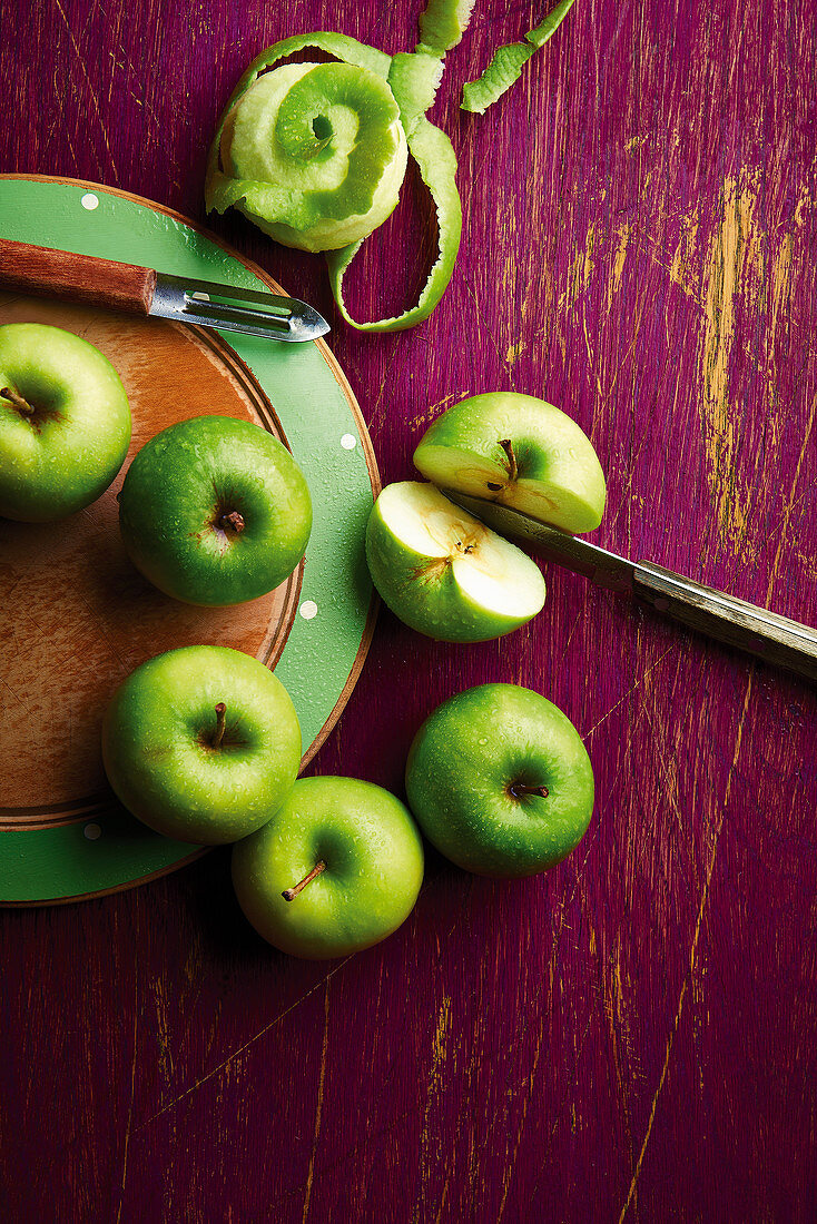Green apples peeled, cut and whole, with knife and peeler on a chopping board