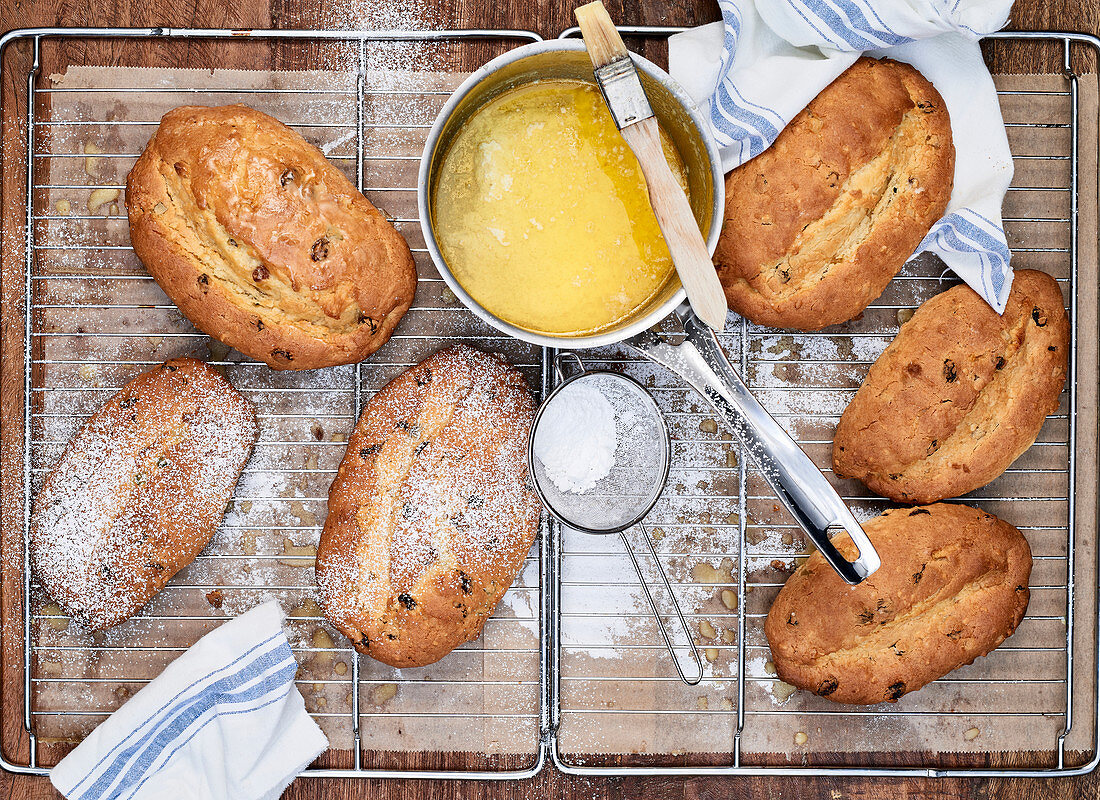 Mehrere Christstollen mit zerlassener Butter und Puderzucker auf Abkühlgitter