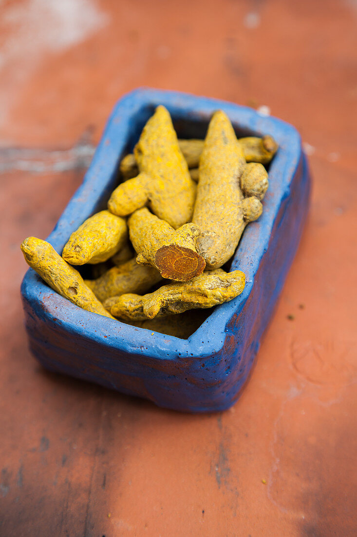 Dried turmeric roots in a blue ceramic bowl