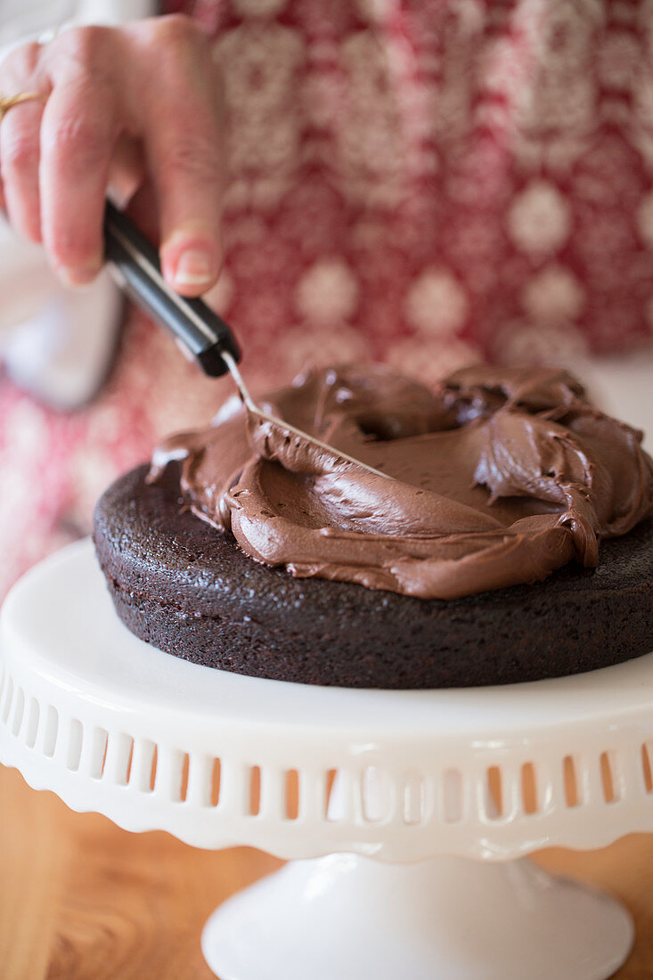 A cake being made: chocolate cream being spread onto a cake base