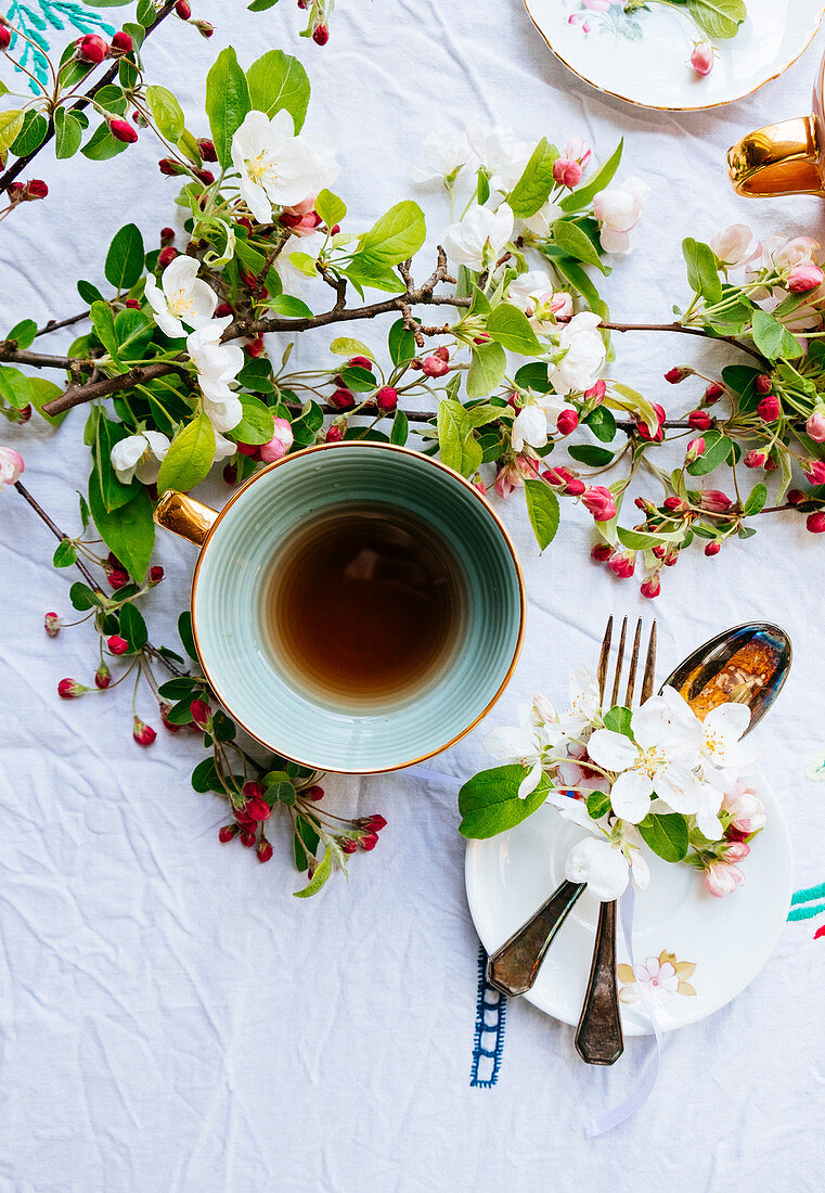 Green cup of tea with blossom on the table and cutlery