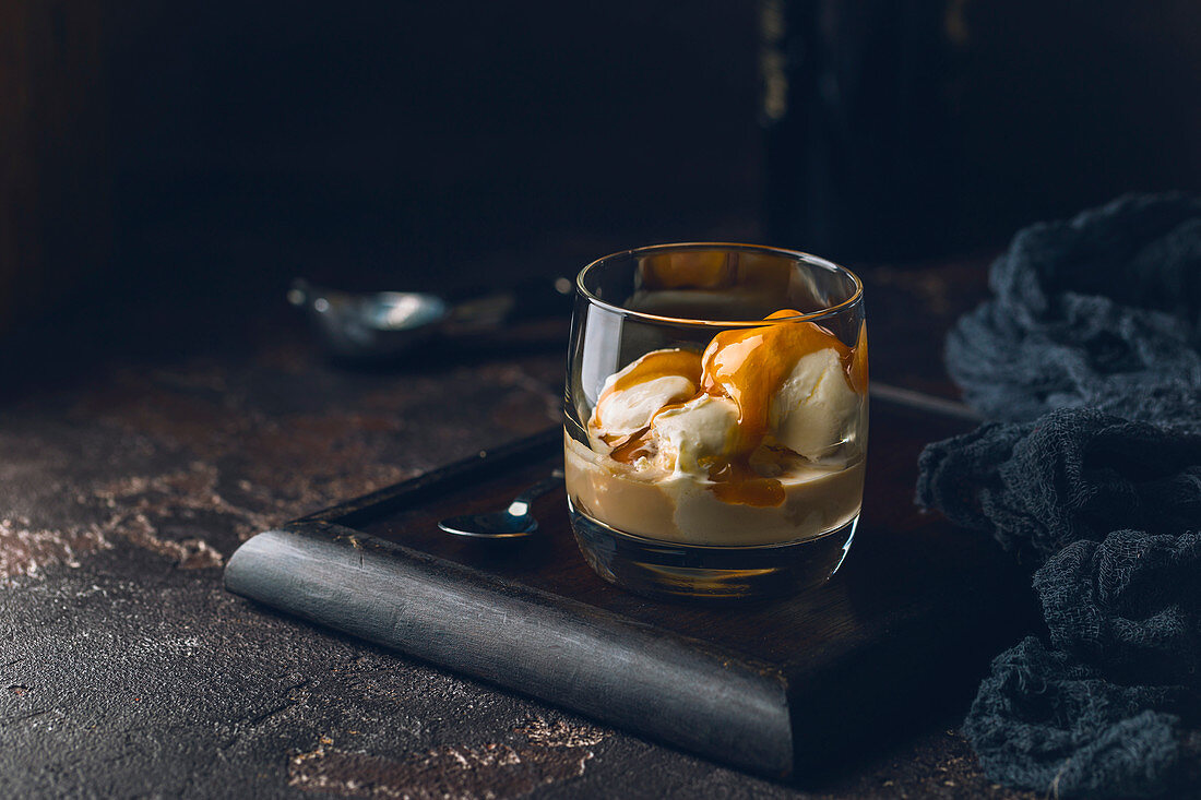 Ice cream with caramel topping and Irish cream liqueur in a glass over dark background