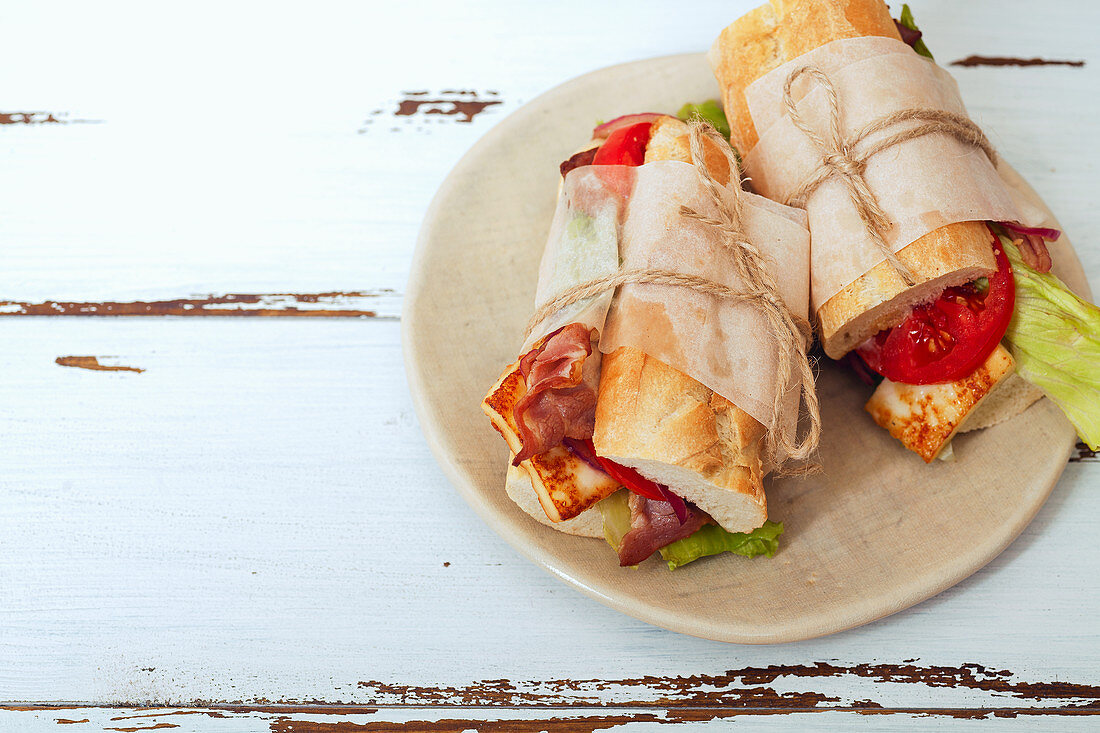 Fresh baguette sandwiches bahn-mi styled with bacon, roasted cheese, tomatoes and lettuce