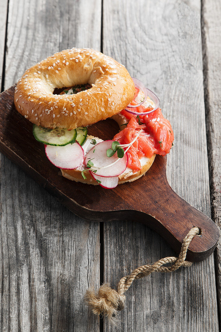 Bagel mit Lachs, Frischkäse, Gurken und frischen Radieschen auf Holzuntergrund