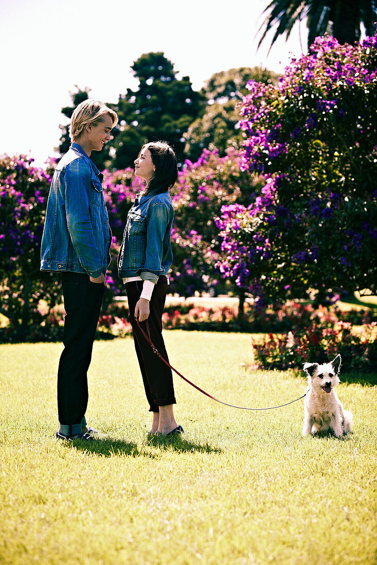 Junges Pärchen im Partner-Look (Jeansjacke und schwarze Hose) im Park, mit Hund