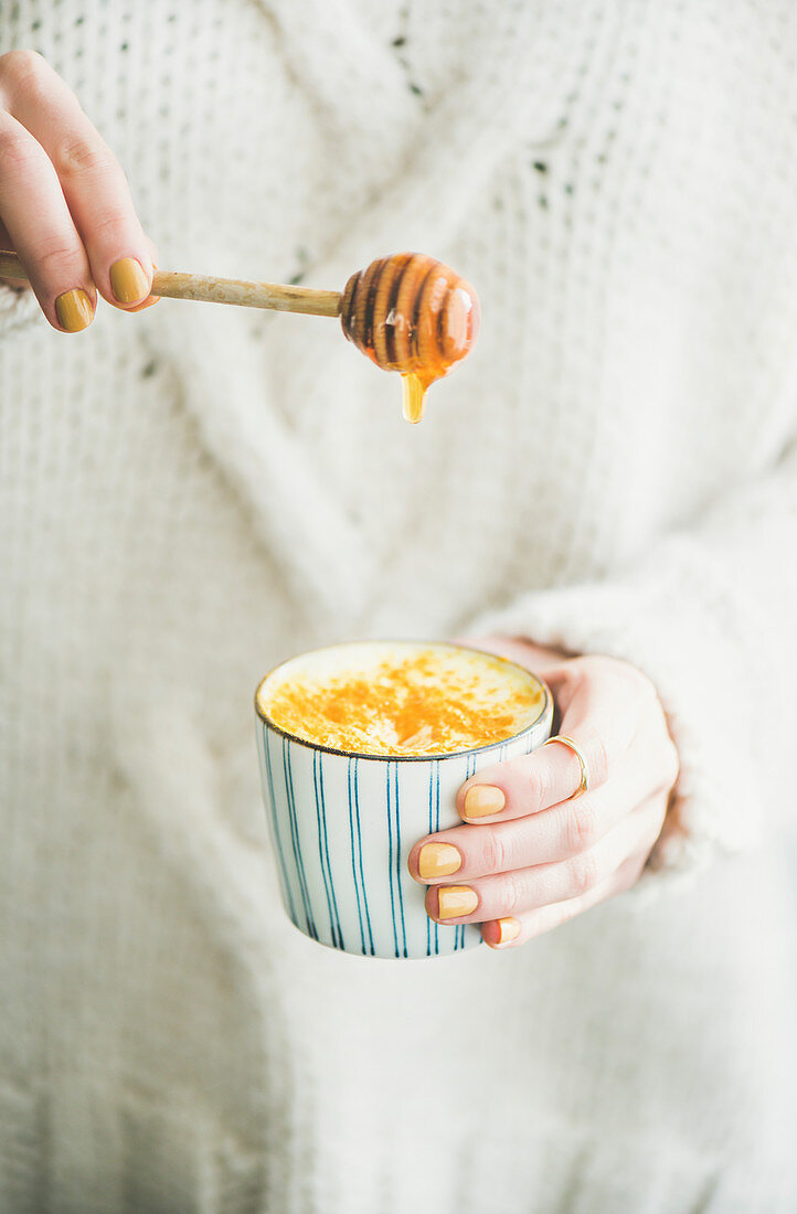 Frau süsst Kurkuma-Latte (Goldene Milch) mit Honig