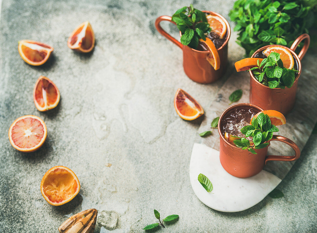 Blood orange Moscow mule alcohol cocktails with fresh mint leaves and friots and ice in copper mugs