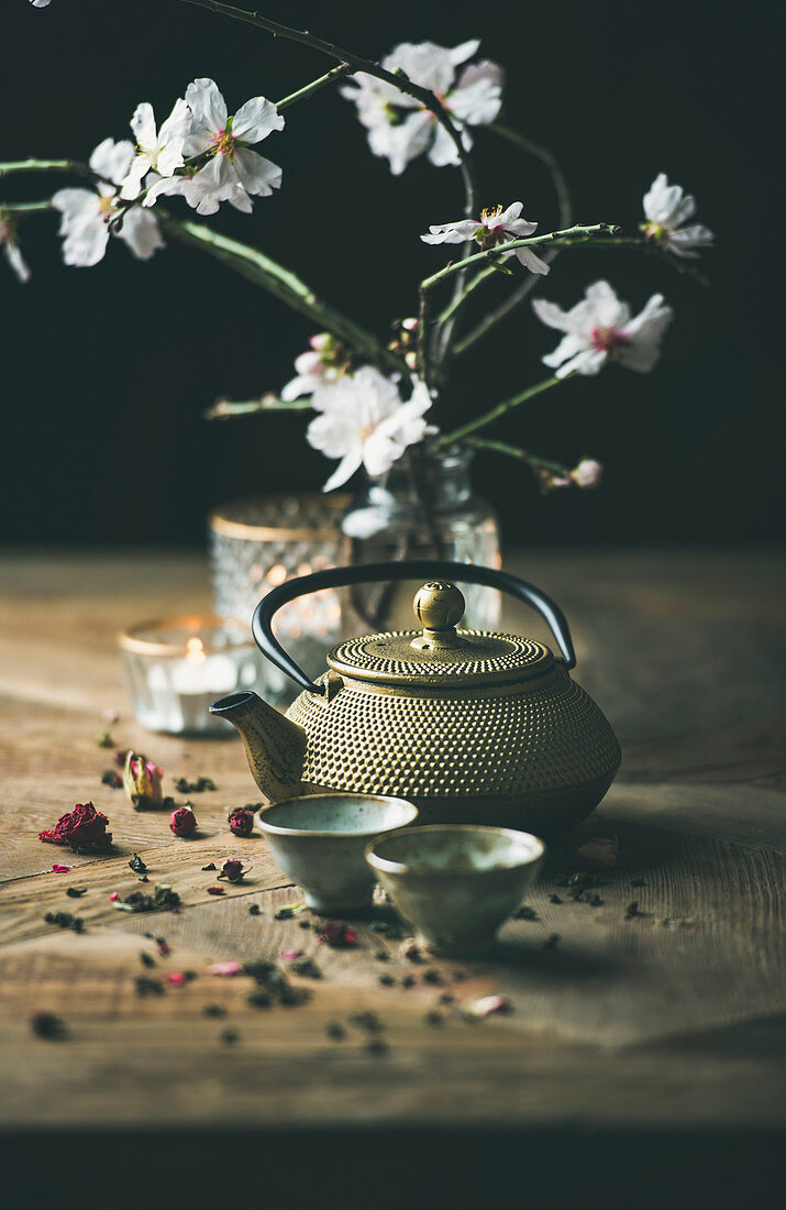 Traditional Asian tea ceremony arrangement with golden iron teapot, cups, candles and almond blossom flowers
