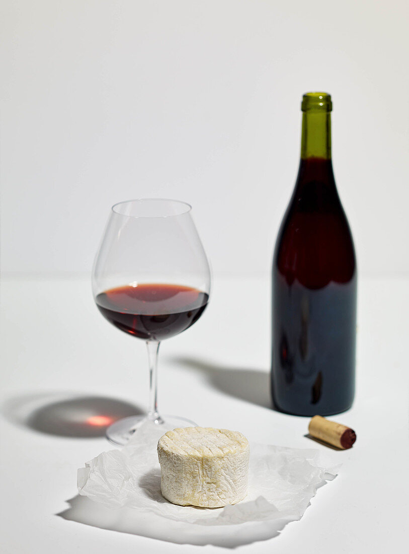 Soft cheese, a glass of red wine, a bottle of red wine and a cork