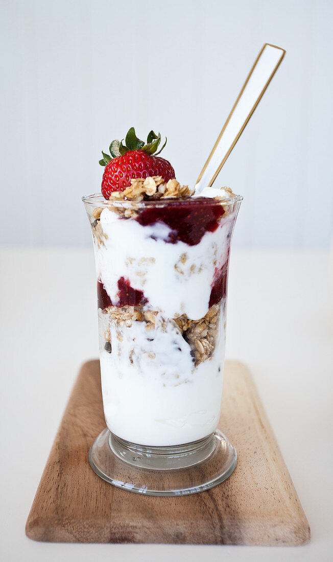 Parfait mit Granola, Vanillejoghurt und Erdbeermarmelade auf Holzbrett