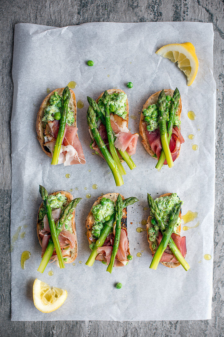Slices of grilled ciabatta with crushed peas, ham and asparagus
